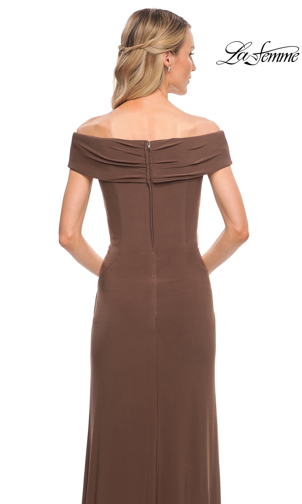 A blonde woman with loose waves models the Long Formal Dress: La Femme 27959—an off-shoulder, brown, floor-length jersey gown—photographed from the back on a white backdrop.
